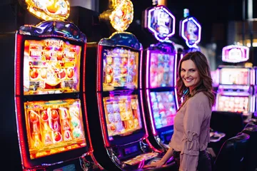 4777GEM Slots — Thousands of thrilling machines await A woman smiling by bright slot machines showing lucky symbols, showcasing the exciting slot offerings at 4777GEM.
